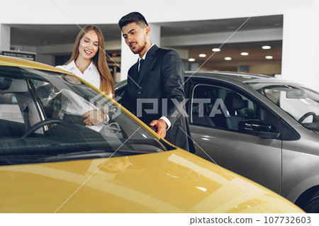 Man car dealer showing a woman buyer a new car Man car dealer showing a woman buyer a new car 107732603