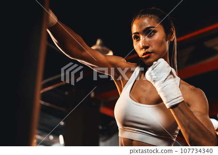 Asian female Muya Thai boxer training, wrapped hand punching. Impetus Asian female Muya Thai boxer training, wrapped hand punching. Impetus 107734340
