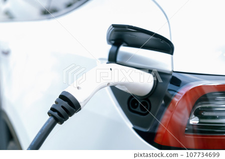 Closeup EV charger plug handle attached to electric vehicle port. Synchronos 107734699