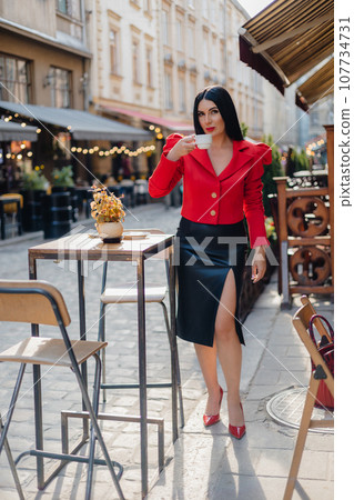 Stunning woman taking sip of coffee in street cafe on pedestrian part of city Stunning woman taking sip of coffee in street cafe on pedestrian part of city 107734731