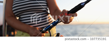 Woman in striped t-shirt enjoys fishing with rod on boat 107735191