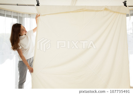 A woman hangs sheets to dry indoors. A woman hangs sheets to dry indoors. 107735491