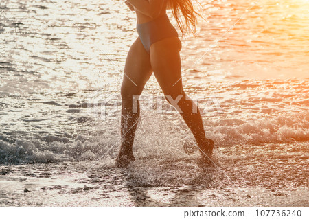 Running woman on a summer beach. A woman jogging on the beach at sunrise, with the soft light of the morning sun illuminating the sand and sea, evoking a sense of renewal, energy and health. 107736240