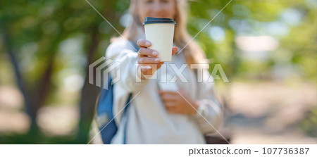 Portrait of cute woman in with cup of coffee overlooking park. Outdoor photo of relaxed female student enjoying hot drink in summer park. 107736387