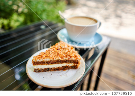 Cup of hot Peanut latte and Carrot pie. The table in the coworking space of the coffee shop. A cup of coffee on the veranda on a sunny day. Coffee break at the cafe. Close-up 107739510