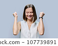 Young cheerful woman clenching her fists on gray background 107739891