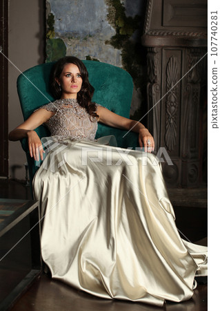 Attractive brunette woman in silky evening gown resting indoor, fashion portrait 107740281