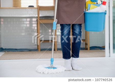 Woman, housewife holding mop and bucket of cleaning materials. 107740526