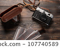 Vintage film camera with leather case and photographic film on dark wooden table. The view from the 107740589