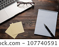 Laptop with glasses on it, a notebook with a pen, and notes on a dark wooden table. Close up for 107740591