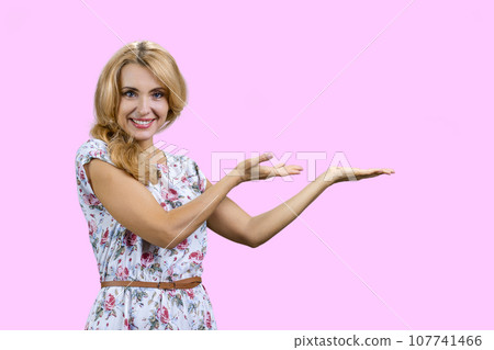 Happy caucasian woman shows copy space with both hands. Isolated on pink. 107741466
