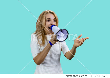 Attractive expressive blonde woman screaming in megaphone. Isolated on turquoise. 107741678