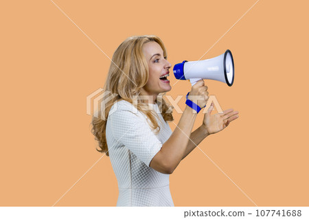 Attractive mature blonde woman screaming in megaphone. Isolated on beige. 107741688