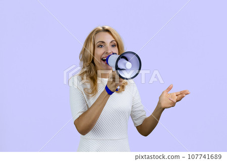 Happy positive blonde woman giving a speech in megaphone. Isolated on purple. Happy positive blonde woman giving a speech in megaphone. Isolated on purple. 107741689