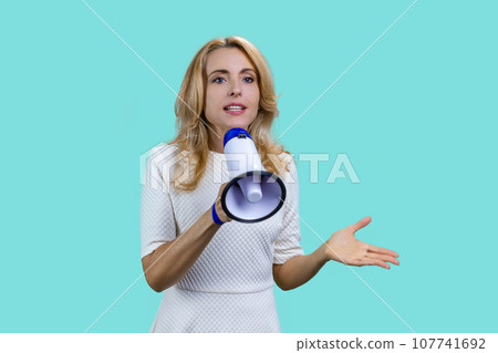 Attractive blonde woman giving a speech in megaphone on colorful background. Isolated on turquoise. Attractive blonde woman giving a speech in megaphone on colorful background. Isolated on turquoise. 107741692