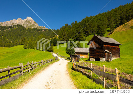 Rustic wooden huts in green valley surrounded by rocky Italian Dolomites Rustic wooden huts in green valley surrounded by rocky Italian Dolomites 107741963