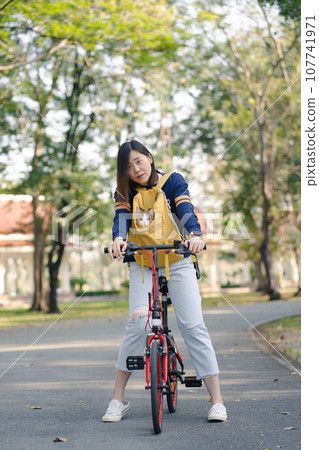 asian woman biking bicycle with her cat in backpack at park 107741971