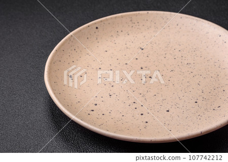Empty round ceramic plate on a dark textured background 107742212