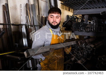 Worker with metal beams during work in workshop Worker with metal beams during work in workshop 107742463