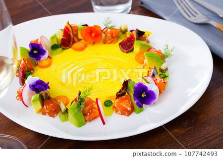 Tasty salmon tartare with ring from fresh vegetables and flowers at plate 107742493