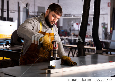 Metalworker drilling steel structures with cordless drill 107742622