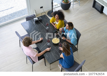 High angle view of multiethnic group of startup friends drinking red wine together at home. High angle view of multiethnic group of startup friends drinking red wine together at home. 107742654