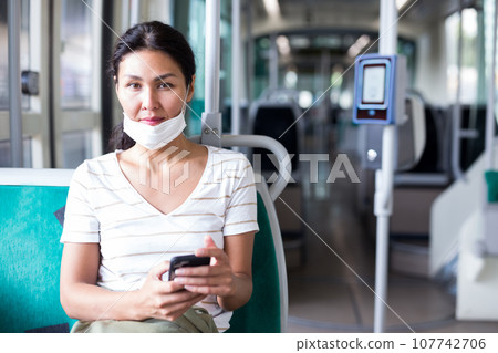Woman in mask with smartphone sitting in tram 107742706