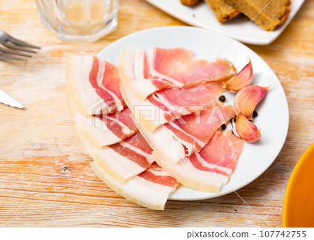 Slices of fresh sliced bacon on a plate Slices of fresh sliced bacon on a plate 107742755