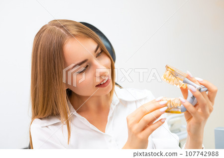 Female with plastic jaw model in the dentist office. 107742988