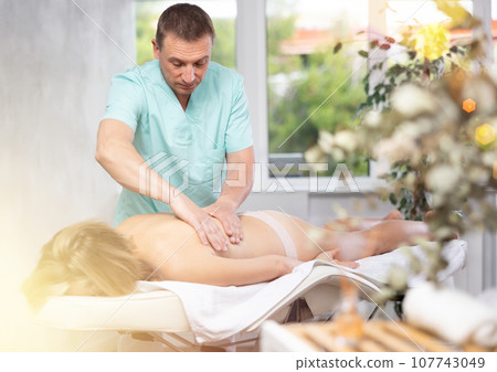 the man gives a massage to the client the man gives a massage to the client 107743049