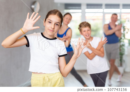 Cheerful friendly school children spreading hands wild apart while practicing active dance with their middle-aged parents in dance hall 107743156