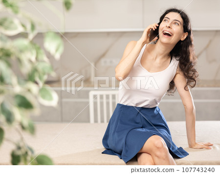 Young woman talking on phone in kitchen 107743240