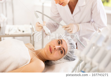 Young woman cosmetologist doing moisturizing procedure to young woman Young woman cosmetologist doing moisturizing procedure to young woman 107743271