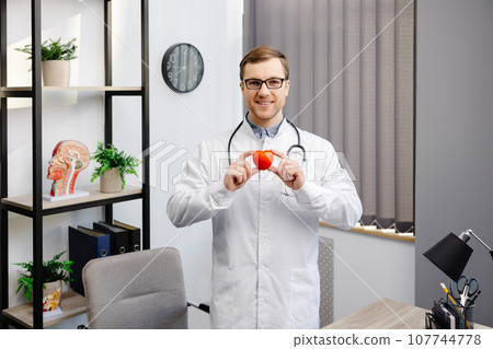 Doctor in white coat and glasses holding a red heart at hospital office. Medical health care and doctor staff service concept 107744778