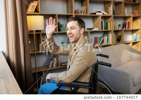 Man on wheelchair in room looking through window and smiling. Side view of young disabled patient in wheelchair looking out window Man on wheelchair in room looking through window and smiling. Side view of young disabled patient in wheelchair looking out window 107744857