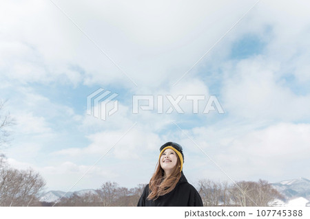 Image of a young woman skiing and snowboarding looking up at the sky at a ski resort Image of a young woman skiing and snowboarding looking up at the sky at a ski resort 107745388