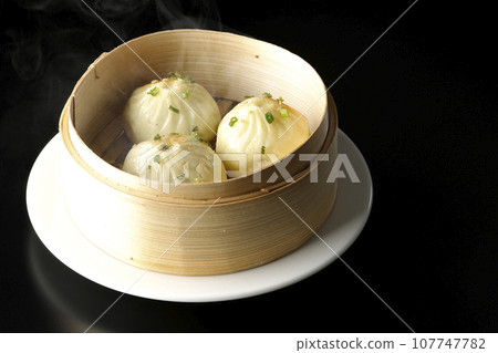 A photo of piping hot xiaolongbao steamed in a steamer against a black background 107747782