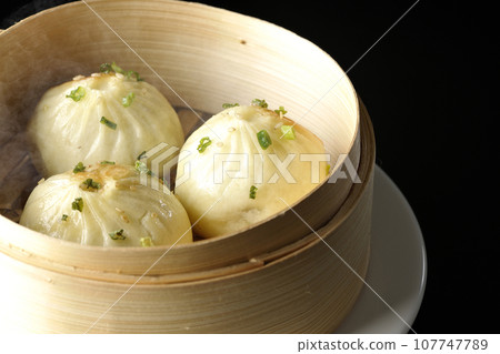 A photo of piping hot xiaolongbao steamed in a steamer against a black background 107747789