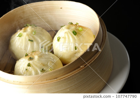 A photo of piping hot xiaolongbao steamed in a steamer against a black background 107747790