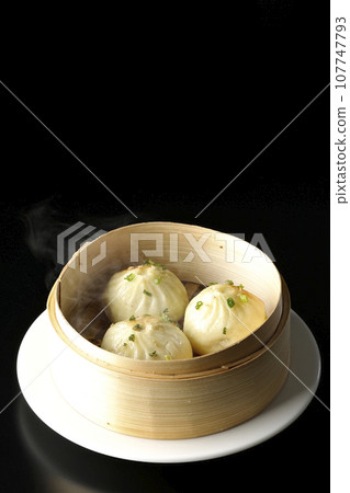 A photo of piping hot xiaolongbao steamed in a steamer against a black background 107747793