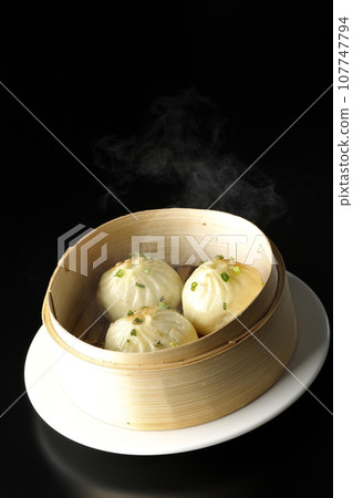 A photo of piping hot xiaolongbao steamed in a steamer against a black background A photo of piping hot xiaolongbao steamed in a steamer against a black background 107747794