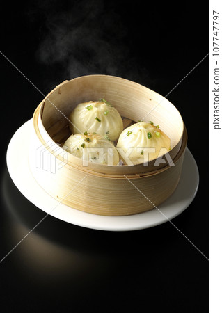 A photo of piping hot xiaolongbao steamed in a steamer against a black background 107747797