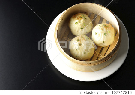 An overhead shot of piping hot xiaolongbao steamed in a steamer against a black background 107747816