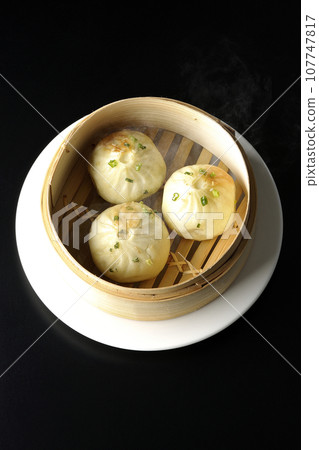 An overhead shot of piping hot xiaolongbao steamed in a steamer against a black background 107747817
