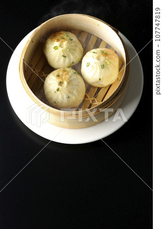 An overhead shot of piping hot xiaolongbao steamed in a steamer against a black background An overhead shot of piping hot xiaolongbao steamed in a steamer against a black background 107747819