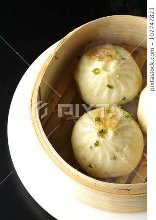 An overhead shot of piping hot xiaolongbao steamed in a steamer against a black background 107747821