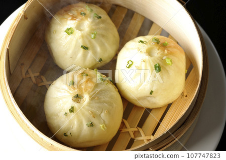 An overhead shot of piping hot xiaolongbao steamed in a steamer against a black background 107747823