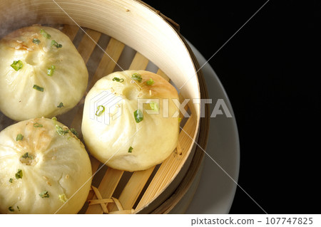 An overhead shot of piping hot xiaolongbao steamed in a steamer against a black background 107747825