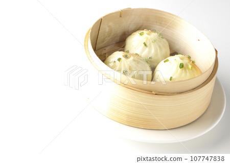 A photo of piping hot xiaolongbao steamed in a steamer against a white background 107747838