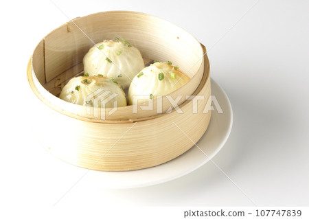 A photo of piping hot xiaolongbao steamed in a steamer against a white background 107747839
